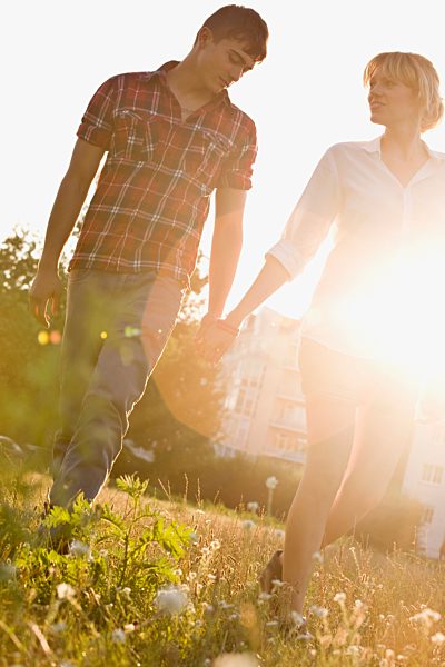 A young couple holding hands walking through a park, front view