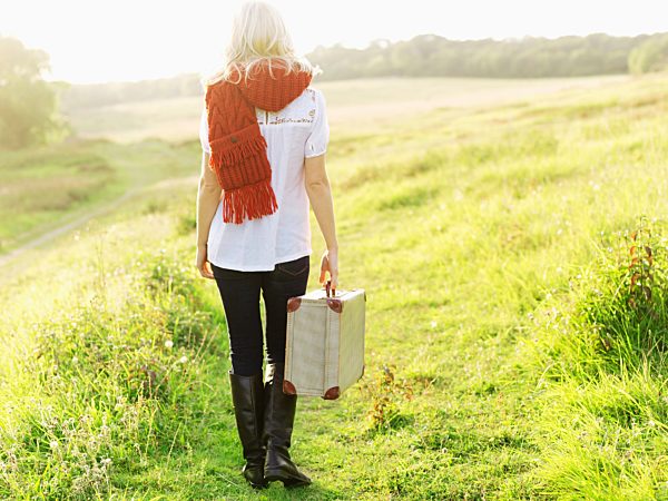 A woman walking in the country carrying a suitcase