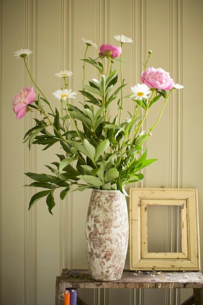 A vase of peonies and daisies and an empty picture frame