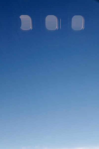 Clear blue sky and windows seen in reflection of airplane window
