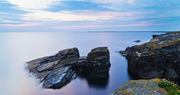 Rock And Tranquil Water Along The Coastline At Dawn; Orkney, Scotland