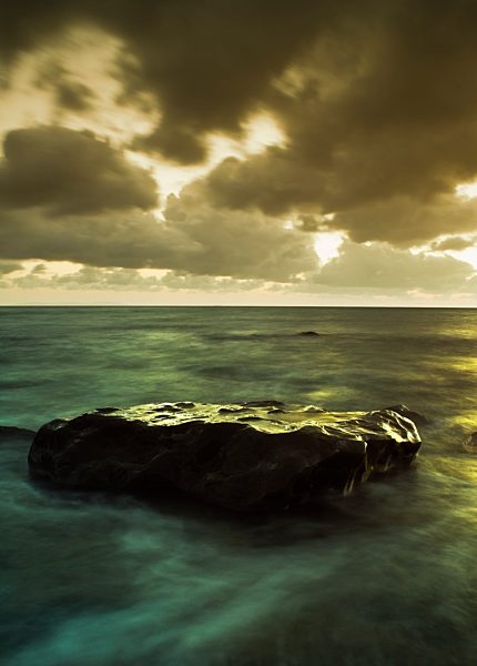 Rock in shallow water under stormy sky