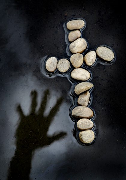 Hand reaching over water for cross made of rocks