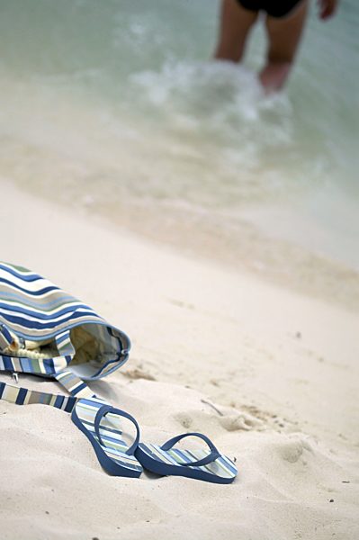 Sandals and Towel Bag on Beach with Woman in Surf