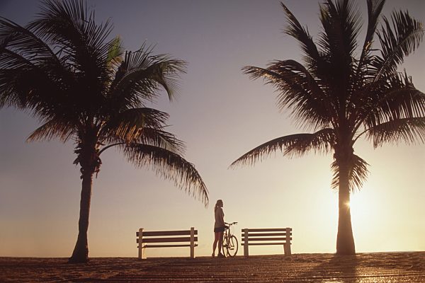 Woman standing with bicycle by palm trees
