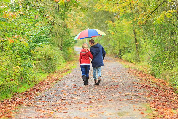 Young couple strolling along country lane with colorful umbrella