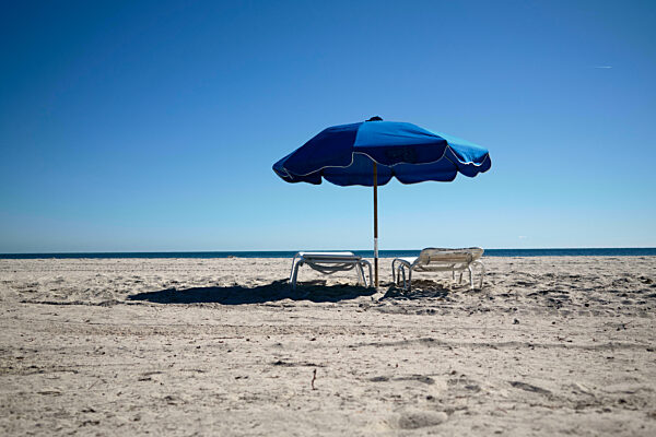 Two lounge chairs and a blue umbrella on a sunny, empty sandy beach under a clear blue sky, Miami, FLorida, USA