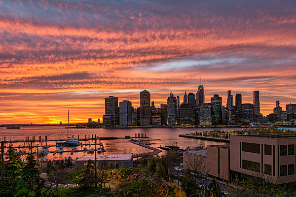 Sunset skyline over city with vibrant orange and pink hues reflected on the water. New York City, NY, USA