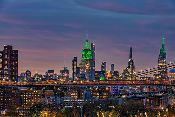New York City skyline with illuminated green skyscrapers and a bridge at twilight. New York City, NY, USA