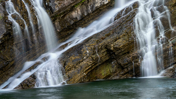 Cascading waterfalls over rugged rocks into a tranquil pool below. Waterton Park, Alberta, Canada