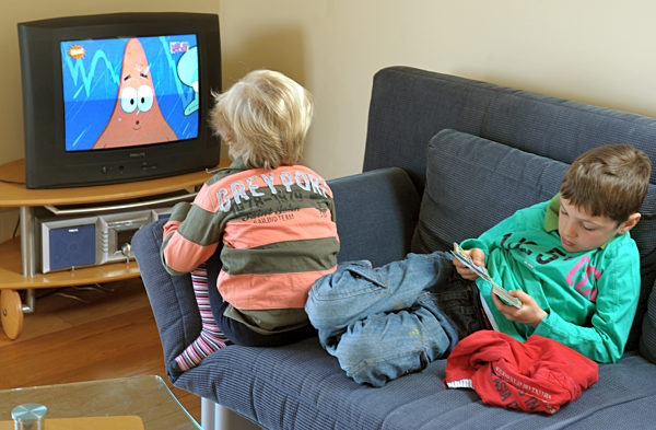 Zwei Kinder sitzen in einem Wohnzimmer vor einem Fernseher und schauen sich...