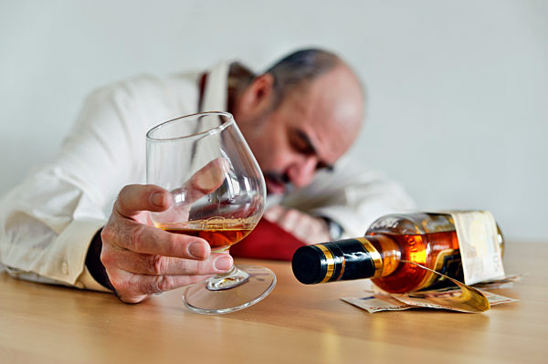 Alkoholiker sitzt mit einem Cognacschwenker und einer Schnapsflasche am Tisch