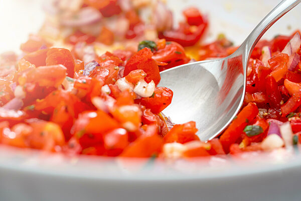 frische geschnittene rote Tomaten, Tomatensalat in einer Schüssel mit einem silbernen Löffel, Nahaufnahme