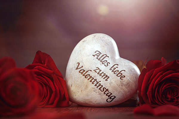rote Rosen und ein Herz aus Stein mit der Aufschrift: Alles liebe zum Valentinstag. Am 14 Februar ist der Valentinstag FOTOMONTAGE