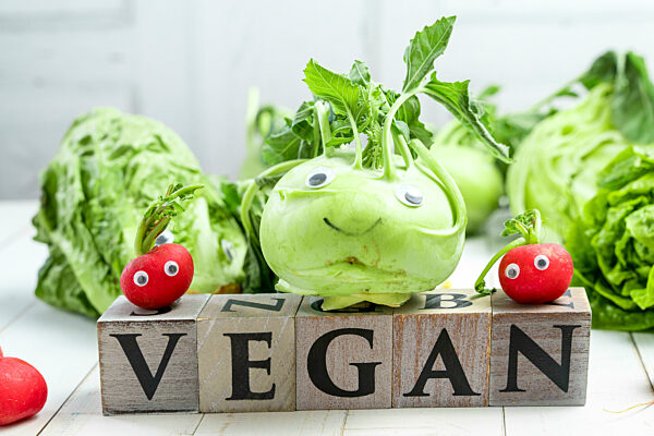 Kohlrabi, Radischen und Salat Gemüse mit Augen und Gesicht und Holzwürfel mit der Aufschrift: Vegan. Glückliches Gemüse, Vegane Ernährung Symbolbild