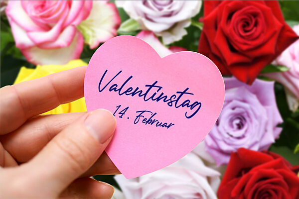 Hand Holding Heart Shaped Note With Inscription Valentine's Day February 14 In Front Of Bouquet Of Roses