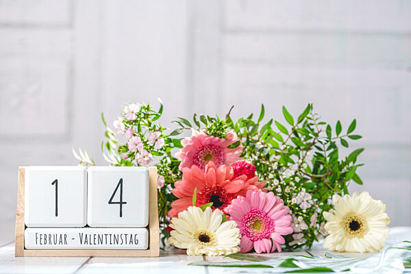 Blumenstrauß mit bunten Blumen und Holzwürfeln mit dem Datum 14 Februar und dem Text: Februar - Valentinstag FOTOMONTAGE