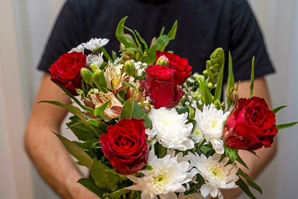 Ein Mann hält einen Blumenstrauß in der Hand mit roten Rosen und weißen Blumen