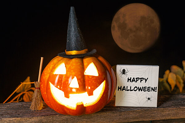 Happy Halloween Gruß neben einem leuchtenden gruseligen Kürbis mit Hexenhut FOTOMONTAGE