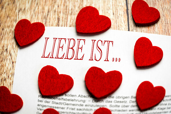Liebesbrief mit vielen roten Herzen auf einem Tisch und dem Text: Liebe ist
FOTOMONTAGE