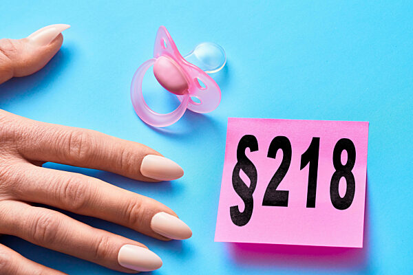 Bavaria, Germany - October 30, 2024: § 218, Paragraph 218 - Abortion, Is Written On A Piece Of Paper Next To A Baby Pacifier And A Woman's Hand. Symbolic Image For Abortion And Abortion During Pregnancy Of Pregnant Women. PHOTOMONTAGE