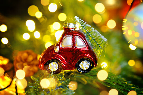 Weihnachtsschmuck in Form eines Autos mit Weihnachtstanne hängt an einem Weihnachtsbaum