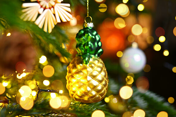 Weihnachtsschmuck in Form einer Ananas hängt an einem Weihnachtsbaum