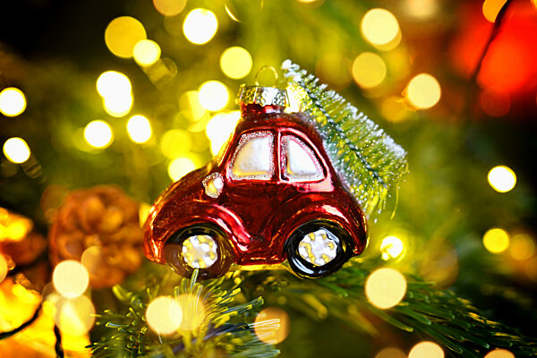 Weihnachtsschmuck in Form eines Autos mit Weihnachtstanne hängt an einem Weihnachtsbaum