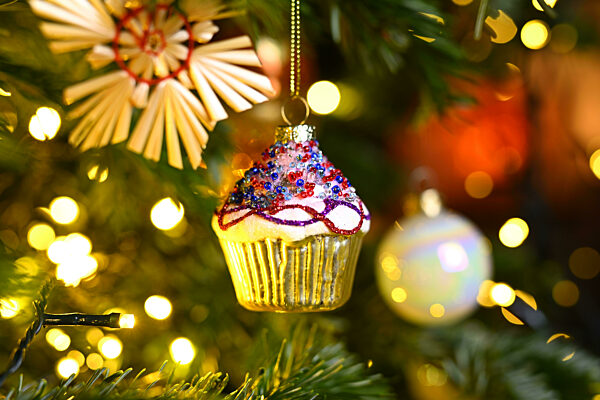 Weihnachtsschmuck in Form eines Cupcakes hängt an einem Weihnachtsbaum