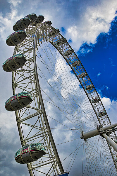 Aufnahme aus der Froschperspektive des London Eye vor einem dramatischen Himmel, die seine Struktur und Gondeln zeigt.