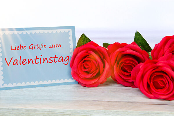 (Fotomontage) Grußkarte mit der Aufschrift LIEBE GRÜSSE ZUM VALENTINSTAG neben roten Rosen