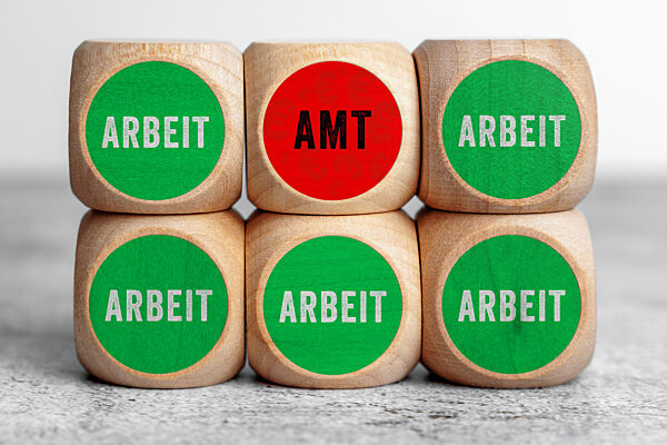 FOTOMONTAGE, Holzwürfel zeigen mehrfach das Wort Arbeit in Grün und einmal Amt in Rot. Das Bild stellt den Gegensatz zwischen Erwerbsarbeit und staatlicher Unterstützung dar und thematisiert Entscheidung, Sicherheit und gesellschaftliche Debatte ob sich