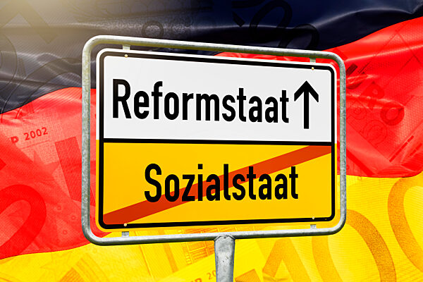 Schild mit Aufschrift Reformstaat und durchgestrichener Aufschrift Sozialstaat vor deutscher Fahne, Fotomontage +++ nur redaktionelle Nutzung