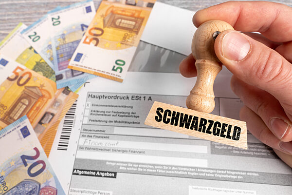 FOTOMONTAGE, Ein Stempel mit der Aufschrift Schwarzgeld wird über eine Einkommensteuererklärung gehalten. Euro-Banknoten daneben symbolisieren illegale Einnahmen, Steuerhinterziehung und die Schattenwirtschaft im Zusammenhang mit Bargeld und Steuer