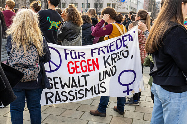 Demonstration in Augsburg zum Internationalen Frauentag (Frauenkampftag, Weltfrauentag). Demonstranten halten ein Banner mit der Aufschrift: Für Frieden, Gegen Krieg, Gewalt und Rassismus