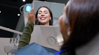 Professioneller Zahnarztpatient, der nach erfolgreicher Zahnaufhellungsbehandlung sein verändertes Lächeln im Spiegel der Klinik überprüft, was Zufriedenheit und Vertrauen in die Ergebnisse der Mundgesundheit widerspiegelt