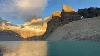 Sonnenaufgang an einem Bergsee mit beeindruckenden Berggipfeln, Touristen am türkisfarbenen See Lago Torres, Aussichtspunkt Mirador Las Torres Base mit den drei Felsnadeln, Alpenglühen an den Felstürmen Torre Sur, Torre Central und Torre Norte, Nationalpark Torres del Paine, Patagonien, Chile