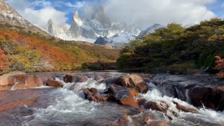 Bachlauf zwischen herbstlich verfärbte Büsche, Ausblick auf Berggipfel Monte Fitz Roy mit Schnee, traumhafte Berglandschaft im Herbst, Nationalpark Los Glaciares, Patagonien, Santa Cruz Provinz, Argentinien