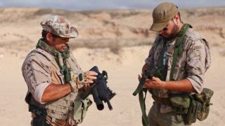 Zwei männliche Militärsoldaten nehmen an Kampftrainingsübungen in einer Wüstenumgebung teil und zielen dabei auf Gewehre mit fokussiertem Gesichtsausdruck