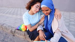 Ein zärtlicher Moment zwischen einem lesbischen Paar, das ein Selfie macht, von denen eine Muslim ist und Liebe und Vielfalt feiert. Ihre Umarmung symbolisiert multikulturelle Einheit und LGBTQIA+ Stolz