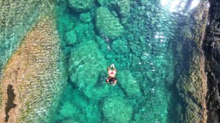Blick von oben auf eine nicht wiederzuerkennende Frau, die gemächlich in den kristallklaren, natürlichen Pools von Aguas Verdes auf Fuerteventura schwimmt. Diese ruhige Szene fängt die lebendigen Farben und die ruhige Umgebung der Kanarischen Inseln ein