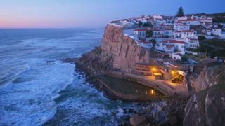 Das Küstendorf Azenhas do Mar in Portugal liegt auf einer Klippe am Atlantik. Das Abendlicht spiegelt sich auf dem Wasser und hebt die Häuser und die Landschaft entlang der Küste hervor