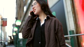 Tiefwinkelaufnahme einer lächelnden jungen Führungskraft, die glücklich auf ihrem Smartphone spricht, während sie in einer geschäftigen Metropole die Treppe von einer U Bahnstation hinaufgeht und vor Freude kommuniziert