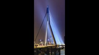 Zeitraffer des Straßenverkehrs in Rotterdam auf der Erasmusbrücke über Nieuwe Maas in der Nacht beleuchtet. Rotterdam, Niederlande. Effekt zum Herauszoomen der Kamera