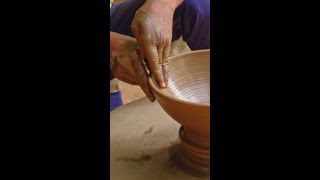 Geschickte nasse Töpferhände, die den Ton auf der Töpferscheibe formen und die Vase formen. Herstellung traditioneller, handgefertigter indischer Schalen, Gläser, Kanne. Shilpagram, Udaipur, Rajasthan, Indien