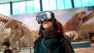 Junge Frau nutzt ein Virtual Reality Headset, um eine interaktive Ausstellung mit prähistorischen Tierskeletten und Fossilien in einem modernen Naturkundemuseum für ein immersives Lernen zu erleben