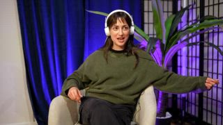 Junge Podcasterin mit Kopfhörern spricht und gestikuliert ausdrucksstark, während sie eine Audioshow aufnimmt. Sie sitzt in einem Sessel in einem modernen Studio zur Erstellung von Inhalten mit blauen und lila Lichtern