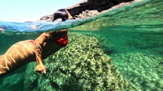 Frau schwimmt im klaren türkisfarbenen Wasser der natürlichen Schwimmbäder Aguas Verdes auf Fuerteventura auf den Kanarischen Inseln, aufgenommen in Echtzeitbewegung