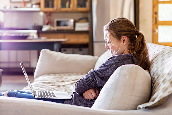 Home,United States,Teenage girl looking at laptop on sofa