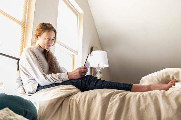 Home,United States,Teenage girl lying in bed using her smart phone